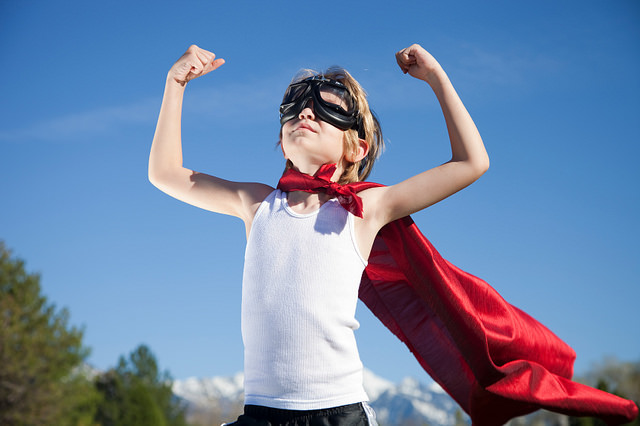 A young boy acting confident in a cape and eye googles.